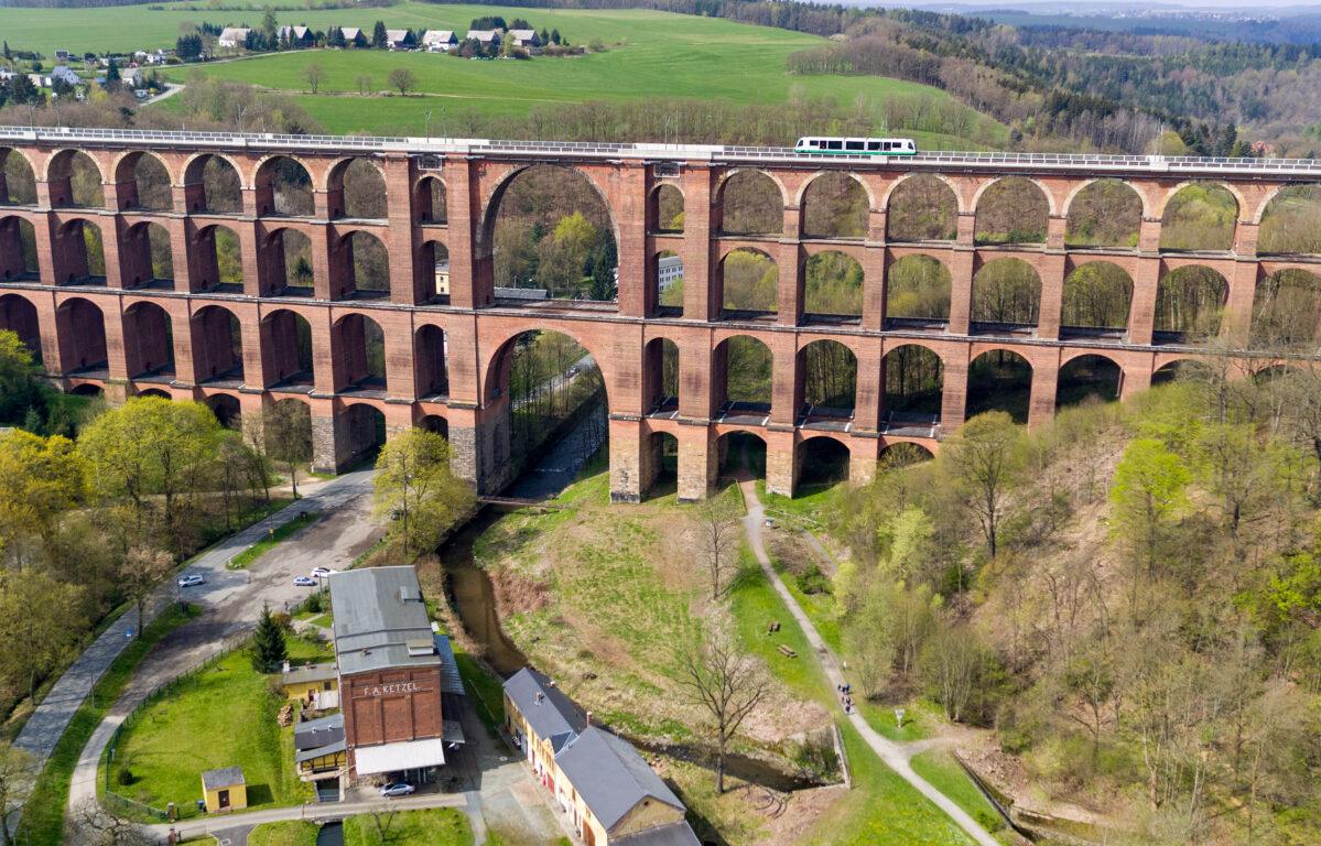 Ein Zug fährt am 21.04.2017 über die Göltzschtalbrücke in Netzschkau (Sachsen) (Luftaufnahme mit einer Drohne). Besucher können das Wahrzeichen der Ingenieurbaukunst jetzt wieder in ihrer ganzen Größe bewundern. In den letzten Monaten wurde der Wildwuchs an Sträuchern und Gestrüpp beschnitten, so dass jetzt wieder vier statt nur noch zwei Etagen der Ziegelbogenbrücke zu sehen sind. Das Bauwerk aus 26 Millionen Ziegelsteinen überspannt in einer Höhe von 78 Metern und auf einer Länge von 574 Metern zwischen Reichenbach und Netzschkau das Tal des Flüsschens Göltzsch. Foto: Jan Woitas/dpa-Zentralbild/dpa ++ +++ dpa-Bildfunk +++