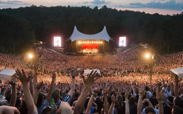 Menschenmassen bei einem Konzert in der Waldbühne Berlin, mit erhobenen Händen vor der Bühne mit markanter weißer Zeltdachkonstruktion